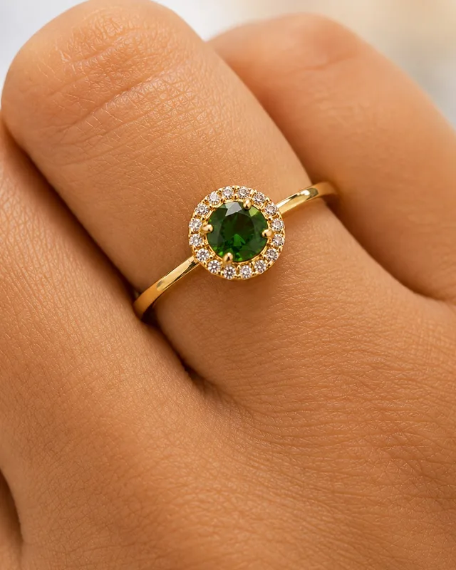 Anel de formatura em ouro 18k na mão, com pedra verde redonda e aro cravejado ao redor